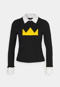 Pull noir avec un dessin de couronne jaune sur le devant, doté d'un col blanc et de poignets blancs contrastants. Texture en tricot et coupe ajustée.