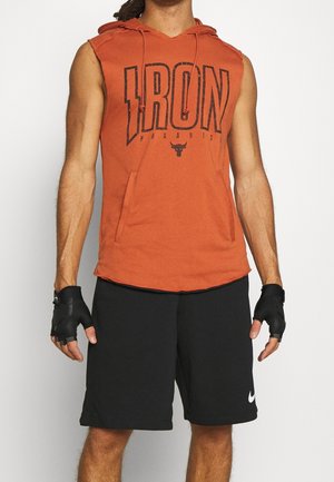 Felpa senza maniche arancione con cappuccio e la scritta "IRON" stampata in nero, dotata di tasca a marsupio. Abbinata a pantaloni corti neri e guanti senza dita.