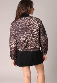 Leren bomberjack met luipaardprint in satijnen stof, voorzien van een zwarte kraag en elastische zoom. Het model draagt een zwarte rok en straalt een casual stijl uit.