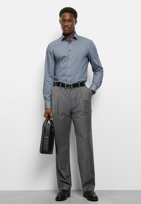 Herren-Business-Outfit mit einem blauen karierten Langarmhemd, grauen plissierten Hosen und einer schwarzen Lederaktentasche.