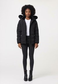 Zwarte pufferjack met een faux fur-voering in de capuchon, gestikte ontwerp en een ritssluiting aan de voorkant. Gecombineerd met zwarte skinny jeans en enkellaarsjes.