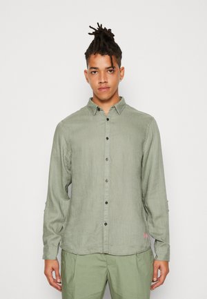 Camisa de manga larga verde claro con cierre de botones en el frente, textura sutil, botones negros y un logo de marca rosa en el dobladillo.