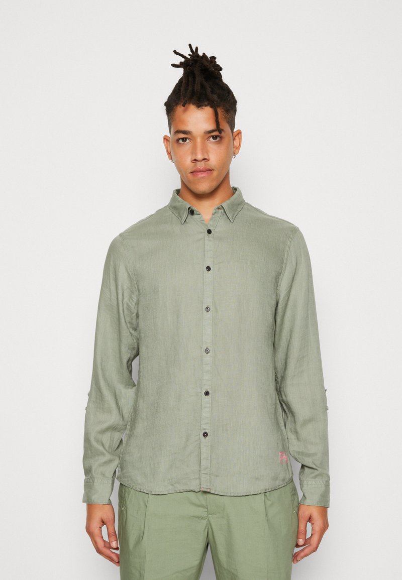 Camisa de manga larga verde claro con cierre de botones en el frente, textura sutil, botones negros y un logo de marca rosa en el dobladillo.