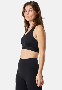 Musta urheilbra, jossa on V-pohjamuotoilu, valmistettu sileästä kankaasta. Ominaisuuksiin kuuluu leveä vyötärönauha, jossa on kohotettua tekstiä alareunassa, sekä paksut olkaimet.