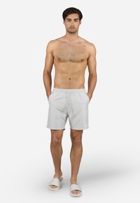 Bañador gris claro con cintura elástica y cordón ajustable. El modelo está descalzo, usando sandalias blancas tipo slider. Tela suave y ligera.