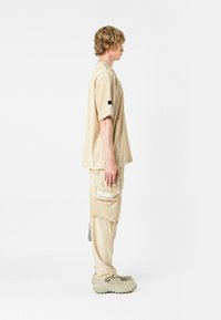 Camiseta de corduroy beige y pantalones a juego, con un bolsillo lateral, mangas cortas y tejido texturizado. Llevado con zapatos tipo slip-on de color gris claro.