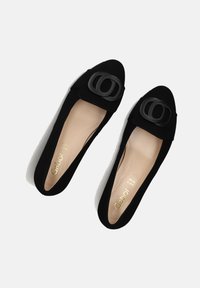 Zwarte suède platte schoenen met een puntige neus, voorzien van een grote zwarte gesp aan de voorkant en een beige binnenzool met gouden merkopdruk.