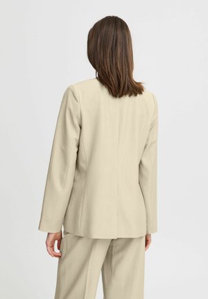 Blazer beige sartoriale dal design elegante, con uno spacco singolo, maniche lunghe e una texture di tessuto liscia. Indossato con pantaloni abbinati.