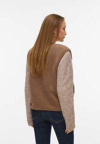 Brown fleece vest with knit beige sleeves, rounded neckline, and textured fabric, featuring a relaxed fit and no visible fasteners.
