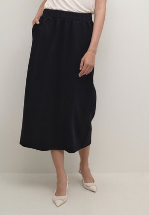 Navy midi skirt with an elastic waistband, side pockets, and a smooth texture. Worn with light-colored pointed-toe heels.