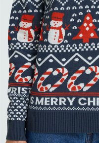 Navy blue knitted Christmas sweater featuring red snowmen, trees, candy canes, and white geometric patterns. Ribbed cuffs and hem.
