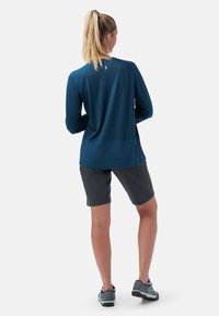 Marineblaues Langarmshirt mit strukturiertem Muster, kombiniert mit grauen Shorts. Das Outfit hat einen lässigen Schnitt und ein praktisches Design.