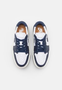 Baskets Nike Air blanches et bleu marine avec boîte à orteils perforée, lacets bleu marine et logos Nike Air visibles sur les semelles intérieures à texture liège, vues de dessus.