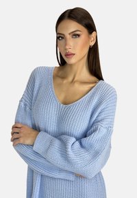 Maglione lavorato a maglia blu chiaro con scollo a V profondo, maniche lunghe e texture a coste. Presenta una vestibilità relaxed e un tessuto morbido.