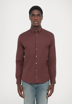 Maroon long-sleeve shirt with a button-down collar, silver buttons, and a tailored fit, paired with light blue jeans. Smooth texture.