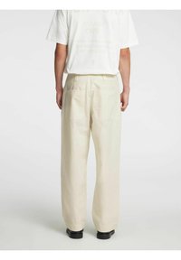 Kremfargede, løstsittende bukser med høyt liv, som har to baklommer og en glatt tekstur, kombinert med en hvit t-skjorte med grafisk trykk.