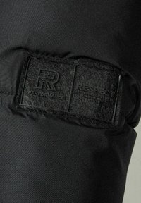 Svart tyg med präglade svarta etiketter med "R PERFORMANCE" och "RESPECT." Slät yta med minimal synlig sömnad.