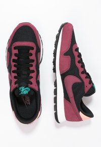 Svarta och mörkrosa Nike Air-sneakers med meshuppsidor, snörning och texturerade sulor visade från ovan- och sidovy.