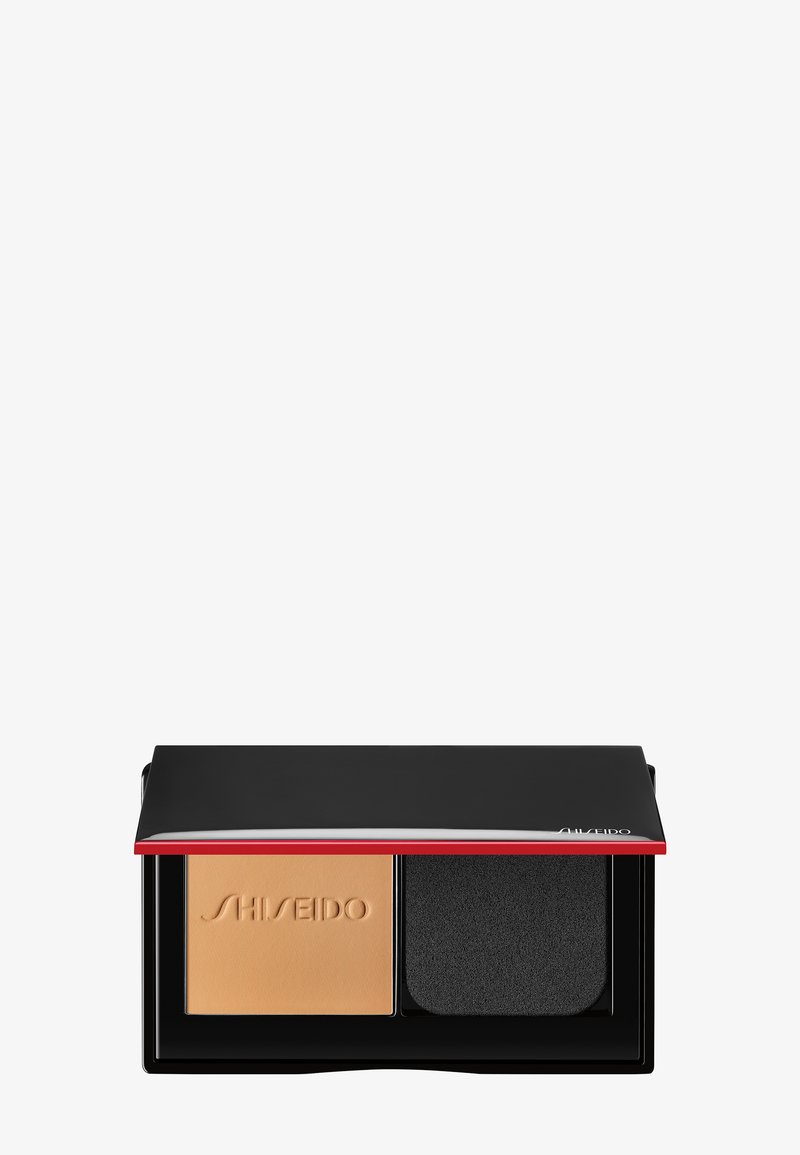 Fond de teint compact avec poudre beige embossée du logo "Shiseido" et éponge applicatrice rectangulaire noire dans un étui noir à bordure rouge.