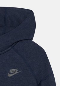 Dark navy hoodie with a smooth texture, featuring a prominent grey Nike logo and contrasting stitching detail along the seams.