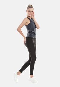 Black leggings paired with a form-fitting dark gray tank top, featuring a round neckline and sleeveless design, worn with white athletic shoes.