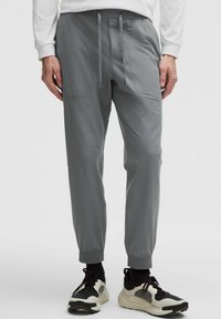 Graue Sporthosen mit elastischen Bündchen und einem Kordelzugbund. Hergestellt aus glattem, leichtem Material; verfügen über seitliche Taschen und ein figurschmeichelndes Design.