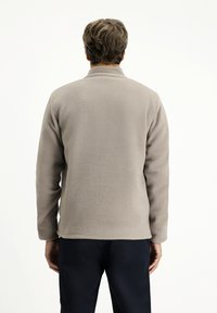 Beige Fleece-Jacke mit Stehkragen, langen Ärmeln und glatter Textur. Die Rückansicht zeigt keine sichtbaren Logos oder Muster.