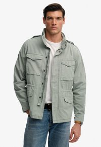 Lysegrøn militærjakke, knappet, med to brystlommer og to nederste lommer med klap. Fremstillet af vævet stof med en stående krave.