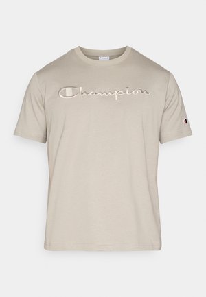 Μπεζ βαμβακερό t-shirt με κοντά μανίκια, που διαθέτει ένα επιβλητικό κεντημένο λογότυπο "Champion" σε ελαφρώς πιο σκούρο τόνο. Κλασικός στρογγυλός λαιμός.