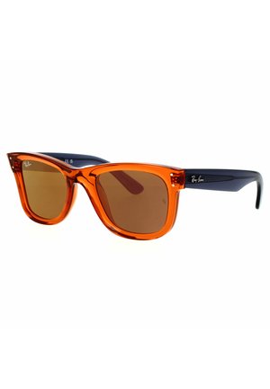 Occhiali da sole con montatura in plastica arancione e lenti marroni. Presentano una forma leggermente cat-eye e asticelle di colore blu scuro a contrasto. Logo Ray-Ban visibile.