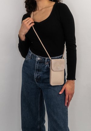 Beige, texturerad axelremsväska med klaffstängning, tunn rem och rektangulär form, bärs tillsammans med en svart topp och högmidjade jeans.