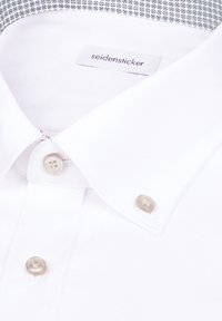 Chemise habillée blanche texturée avec col boutonné et boutons beige, étiquette "seidensticker" visible à l'intérieur du col.