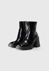Bottes noires en cuir jusqu'à la cheville avec un talon épais et texturé. Elles possèdent une fermeture zippée sur le côté et une finition lisse et brillante. Design de bout légèrement arrondi.