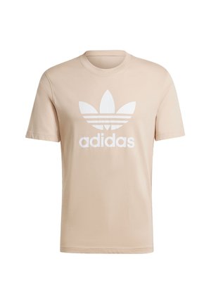 T-shirt in cotone beige chiaro con maniche corte, caratterizzato da una grande grafica bianca del logo a tre foglie e il testo "adidas" sulla parte anteriore.