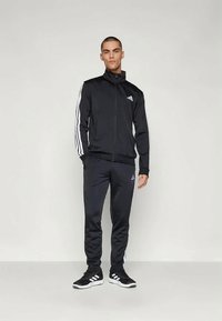 Melns sporta kostīms ar baltām svītrām gar rokām un biksēm. Izgatavots no gludas auduma, satur ar rāvējslēdzēju aizveramu jaku un logo akcentus.