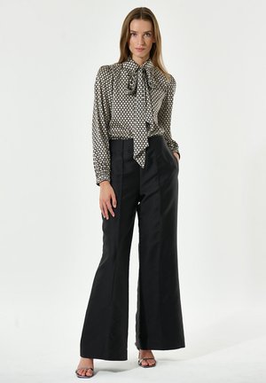 Blusa a righe bianco e nero con fiocco al collo, abbinata a pantaloni neri a vita alta e a gamba larga. Tessuto morbido, vestibilità strutturata.