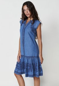 Abito di denim con maniche corte a cappuccio, scollatura a V e gonna svasata. Presenta dettagli ricamati color navy e orlo arricciato.