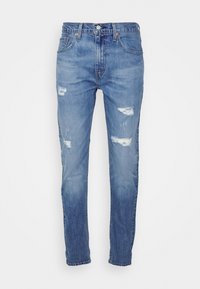 Jeans ajustados de color azul con parches desgastados en los muslos y rodillas, diseño de cinco bolsillos y cierre de botón en la cintura.