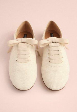 Beige Leinenschuhe mit glatter Textur, runder Spitze und Stoffschnürsenkeln. Mit einer Schleifen-Akzentuierung an der Vorderseite und einer braunen Sohle.