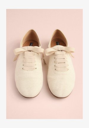 Beige canvas shoes with a smooth texture, round toe, and fabric laces. Features a bow accent on the front and a brown sole.
