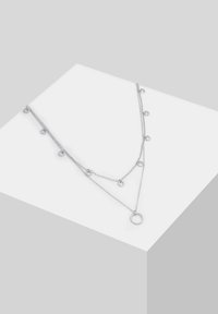 Collana in argento a strati con accenti circolari lungo le catene e un grande pendente ad anello alla base.