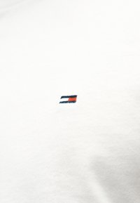 Μικρό κεντημένο λογότυπο με τη σημαία σε κόκκινο, λευκό και μπλε χρώμα, τοποθετημένο στο κέντρο λευκού βαμβακερού υφάσματος, πιθανόν μέρος ενός ρούχου.