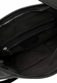 Interiér černé kožené tašky s látkovým podšívkou, zipovou kapsou a kapsou na slipy. Texturovaný materiál s detaily z stříbrného zipu.