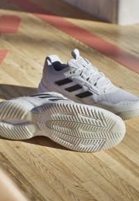 Białe buty sportowe z czarnym, trzema paskami, siateczkowa cholewka, teksturowana podeszwa i wyraźny wzór bieżnika.