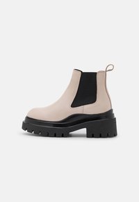 Botas Chelsea de cuero beige con paneles laterales elásticos negros, suela de plataforma gruesa negra y una tira en la parte posterior.