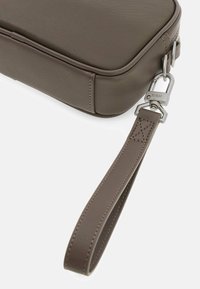 Borsa in tessuto marrone con zip, dotata di gancio in metallo argentato e tracolla coordinata. Bordi arrotondati e design robusto.