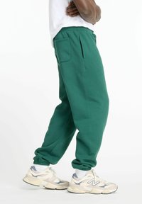 Gröna sweatpants i en bomullsblandning med snörning i midjan, sidofickor och elastiska muddar. Samman med vita och grå sneakers.