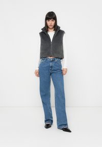 Gilet en polaire gris avec fermeture éclair et capuche, associé à un jean taille haute bleu clair et des ballerines pointues noires. Design minimaliste.