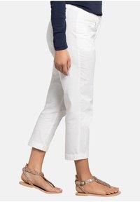 Witte, cropped broek van katoen met een gladde textuur, gecombineerd met platte, strap sandalen met een gevlochten ontwerp en metalen accenten.