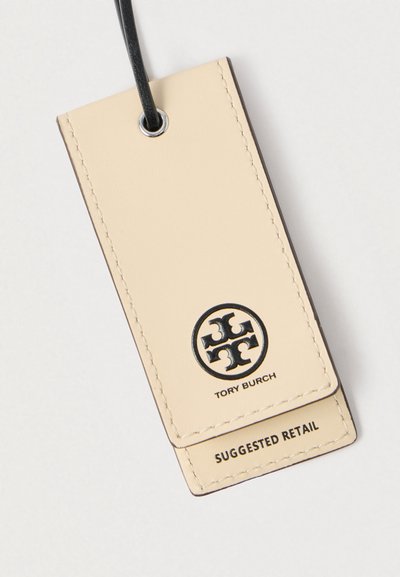 Étiquette en cuir Tory Burch beige clair avec couture noire, présentant un logo et le texte « PRIX DE DÉTAIL SUGGÉRÉ », attachée par un cordon noir.